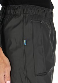 Zwarte waterdichte broek met een elastische tailleband, voorzien van een zijzak met knoopsluiting en een klein Zweeds vlagaccent.