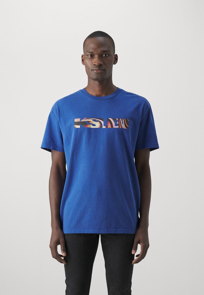 Camiseta de algodón azul con un estampado gráfico rectangular y patrones coloridos en el pecho. Mangas cortas y escote redondo.