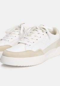 Baskets blanches avec une tige en cuir lisse, des accents en daim beige, un bout rond et une semelle plate en caoutchouc blanc. Présentent des détails perforés et une fermeture à lacets.