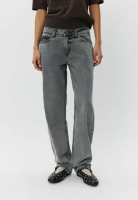 Jeans de mezclilla gris de pierna ancha con una cintura alta, que cuentan con bolsillos frontales, costuras tonales y un acabado desgastado. Zapatos negros y blancos de tipo slip-on.