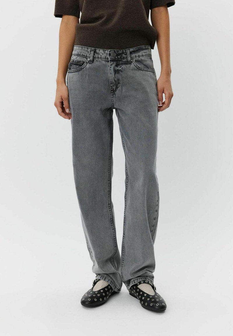 Jeans de mezclilla gris de pierna ancha con una cintura alta, que cuentan con bolsillos frontales, costuras tonales y un acabado desgastado. Zapatos negros y blancos de tipo slip-on.