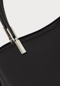 Primer plano de un bolso de cuero negro texturizado que muestra los accesorios de metal plateado del asa sobre un fondo claro.