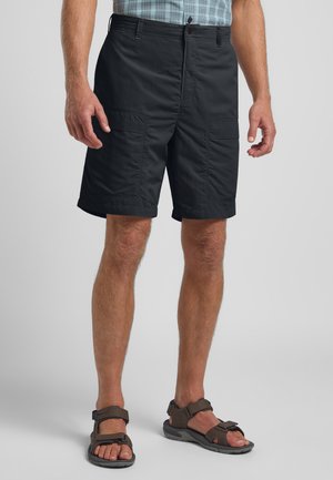 Schwarze Cargo-Shorts aus leichtem Material, mit Vordertaschen und lockerem Schnitt, kombiniert mit braunen Riemchensandalen.