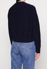 Mörkblå stickad tröja med ribbat nederkant och muddar, som har en avslappnad passform. Kombinera med ljusblå denimjeans med bakfickor.