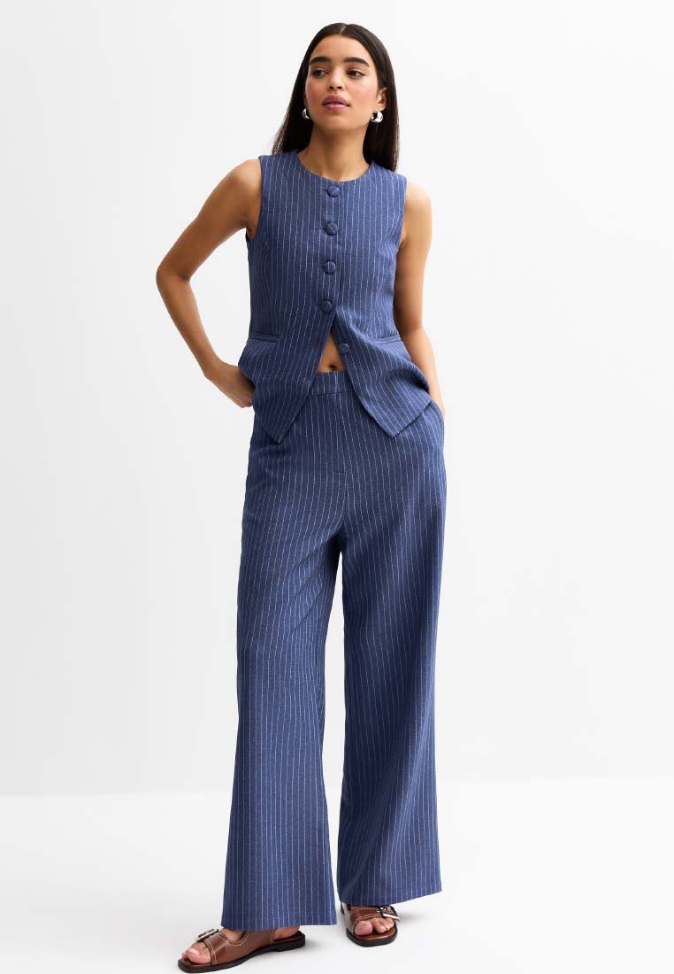 Gilet bleu marine à fines rayures et pantalon large. Le gilet a un col rond et cinq boutons. Tissu lisse avec une coupe ajustée.