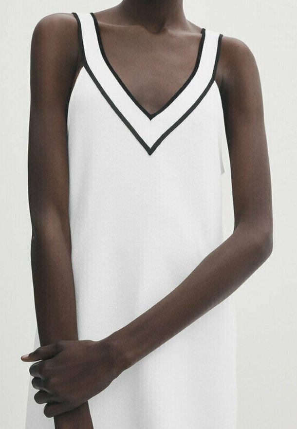 Vestito bianco senza maniche con una scollatura a V profonda, caratterizzato da un bordo nero lungo il collo. Il tessuto appare liscio con una texture a maglia.