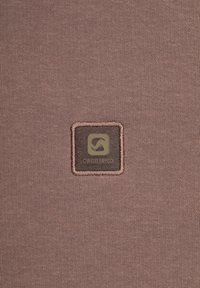 Bruine textuurstof met een vierkant patch met het 'Gabbiano'-logo in een donkere kleur, omgeven door een lichtbruine rand.