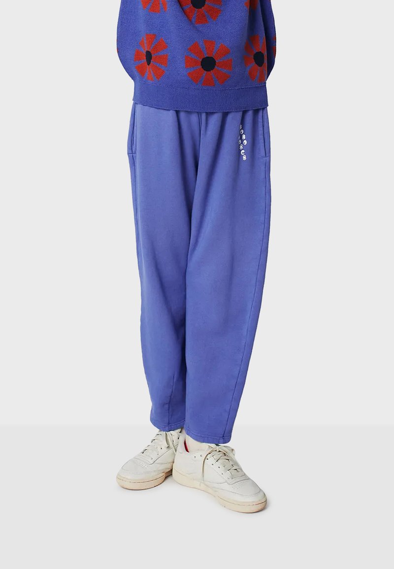 Pantalones de chándal azul con un corte relajado, que cuentan con bolsillos laterales y un sutil detalle del logo. Combinados con zapatillas blancas.