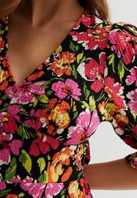 Robe à motif floral avec des fleurs vibrantes roses, oranges et vertes sur un tissu texturé noir. Décolleté en V et manches bouffantes.