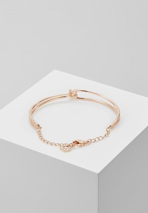 Bracelet fin en or rose avec une chaîne et un fermoir en forme de homard, reposant sur une surface géométrique blanche sur un fond gris clair.