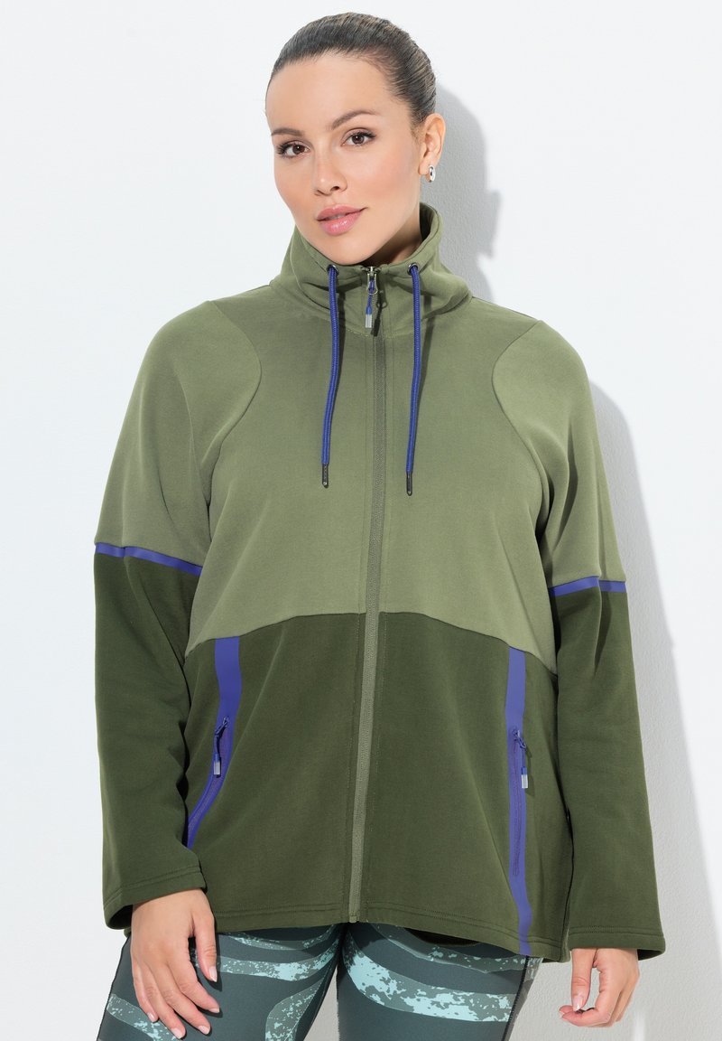 Green zip-up jacket with a high collar, featuring contrasting dark green and blue accents, two side pockets, and a soft textured fabric.