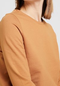 Lange mouwen, rondhals sweatshirt van zacht, lichtgewicht, tan stof. Heeft een gladde textuur met subtiele stiksels.