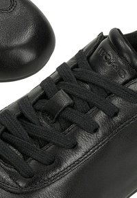 Schwarzer Ledersneaker mit dicken schwarzen Schnürsenkeln, geprägtem Markennamen "wojas" auf der gepolsterten Zunge und detaillierter Nahtverarbeitung an den Seiten.