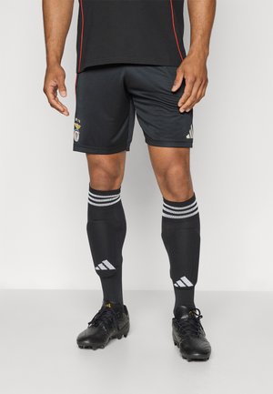 Sorte atletiske shorts med holdlogo, parret med knæ-høje sorte sokker med hvide striber og sorte fodboldstøvler.