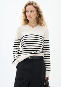 V-neck villapaita, jossa on vaaleanpunainen väri ja mustat vaakaraitat, pitkät hihat, rento istuvuus ja joustavat hihansuut, yhdistettynä mustiin housuihin.