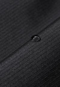 Svart texturerad tyg med ribbat mönster. En klar vattendroppe vilar på ytan och framhäver materialets vattenavvisande egenskaper.