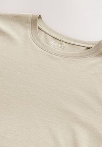 Beiges Baumwoll-T-Shirt mit Rundhalsausschnitt, sichtbarem, genähtem Kragen und leichtem Markenlabel im Nackenbereich.