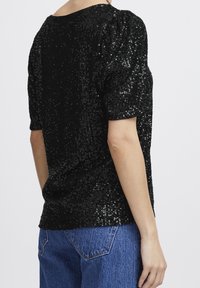 Svart paljettopp med puffiga korta ärmar, slät textur och rundad halsringning, kombinerad med denimjeans.