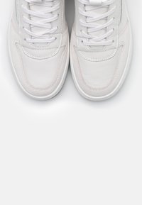 Sneakers bianchi in pelle con lacci, cuciture visibili e suole in gomma, mostrati dall'alto su uno sfondo bianco.