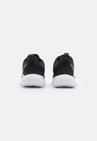 Scarpe da ginnastica nere con tomaia in tessuto texture, dotate di una suola bianca e anelli posteriori per facilitare l'uso. Design semplice senza motivi complessi.