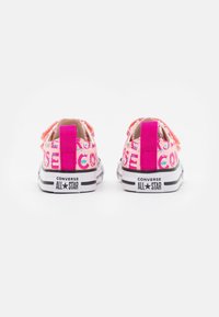 Rosa tygskor med vita detaljer, som har flerfärgade tryck, elastiska remmar och svarta gummisulor.