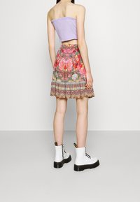 Top sans bretelles lilas, mini jupe à imprimé floral avec des motifs complexes, portée avec des bottines blanches à semelles et lacets noirs.