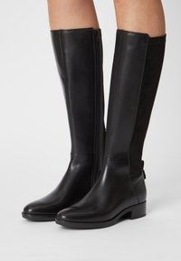 Botas negras hasta la rodilla que combinan cuero liso y ante, con una cremallera lateral, punta redonda y un tacón bajo en bloque.