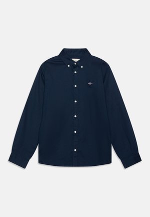 Marinblå skjorta med knappar framtill, långa ärmar, krage och vita knappar; har en liten logotyp på vänster bröst. Tillverkad av bomull, med en mjuk textur.