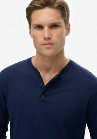 Marineblauw poloshirt met lange mouwen van katoen, met een knoopsluiting en bruine knopen en een klein logo op de borst.