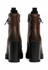 Bottes chelsea en cuir marron avec un talon bloc noir haut, présentant une fermeture éclair sur le côté et une languette à l'arrière. Texture lisse avec des accents minimaux.