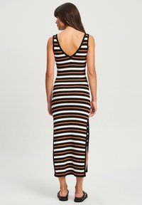 Schwarz-weißer und orange gestreifter Maxikleid mit V-Ausschnitt, gerippter Textur und Schlitzen an beiden Seiten, kombiniert mit schwarzen flachen Sandalen.