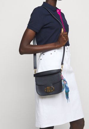 Bolso bandolera de cuero azul oscuro con un cierre de logo dorado, correa ajustable y un accesorio de pañuelo colorido. Textura suave, forma rectangular.