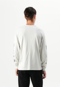 Lange mouwen lichtgrijs t-shirt met een relaxte pasvorm, voorzien van zwarte grafische prints langs de mouwen en een ronde halslijn.