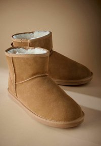 Tamnasti nubuck gležnjači s mekanim plišanim unutrašnjim dijelom. Imaju zaobljeni vrh, laganu potplat i šivane detalje duž šavova.