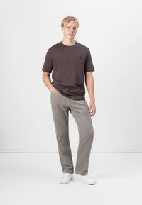 Short-sleeve dark brown t-shirt with a crew neck, paired with light gray pants and white sneakers, creating a casual, modern look.