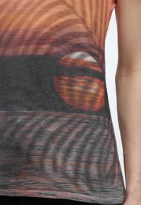 Ύφασμα που απεικονίζει σκηνή ηλιοβασιλέματος με τον ήλιο μερικώς πάνω από τον ορίζοντα, αντανακλάσεις στο νερό και κυματιστά μοτίβα, φορεμένο από άτομο με εκτεθειμένο χέρι.