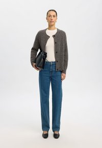 Grijze wolmix cardi met knopen, wit aansluitend topje, blauwe straight-leg jeans en zwarte gestructureerde handtas. Zwarte flats maken de look af.
