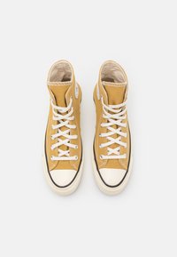 High-top sneakers made of mustard yellow canvas, featuring white laces, a white rubber toe cap, and black trim along the sole.