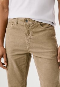 Pantaloni in corduroy beige a taglio dritto, con chiusura anteriore a bottone, passanti per cintura e tasche laterali. Tessuto testurizzato e a coste.