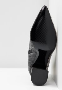 Mustat ja harmaat käärmeennahkakuosiset teräväkärkiset korkokengät, joissa on kiiltävä musta pohja ja teksturoitu korko, jossa on neliskulmainen kanta.