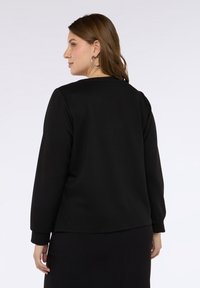 Sweatshirt lungo nero con maniche lunghe e vestibilità rilassata, scollo rotondo e polsini a costine. Tessuto con una texture liscia. Design minimalista senza motivi visibili.