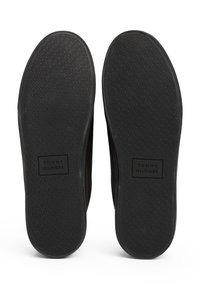 Czarne podeszwy trampków z teksturowaną gumową powierzchnią, z prostokątną naszywką z napisem „TOMMY HILFIGER” na środku. Prosty, płaski design.