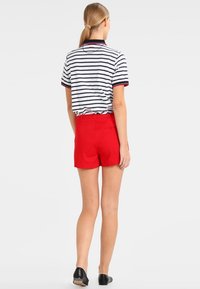 Polo à rayures bleu marine et blanches, short rouge et chaussures plates noires. Le polo possède un col et des manches courtes.