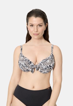 Mujer con cabello largo y oscuro, vestida con un bikini de estampado de hojas en blanco y negro en la parte superior y bikini negro sólido en la parte inferior, mirando hacia adelante.