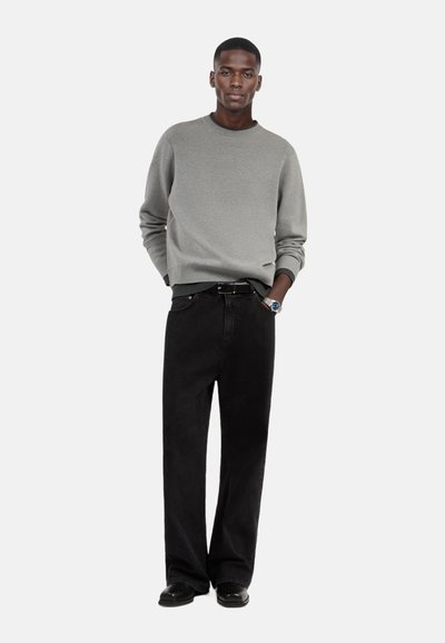 Grauer Pullover mit Rundhalsausschnitt, kombiniert mit schwarzen Cordhosen und schwarzen Schuhen. Das Outfit zeichnet sich durch ein einfaches Design und eine lässige Passform aus.