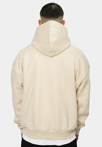 Beige hooded sweatshirt with a relaxed fit, ribbed cuffs, and waistband. Soft texture, minimal design, view from the back.