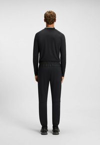 Svart atletisk outfit som består av en långärmad topp och byxor med elastisk midja. Slät textur och minimalistisk design. Svarta sneakers.