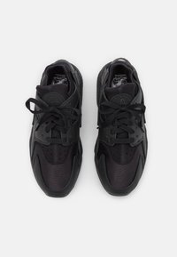 Ett par svarta Nike Huarache-sneakers med snörning, sedd uppifrån mot en enfärgad vit bakgrund.