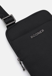 Borsa nera in nylon con superficie testurizzata, dotata di chiusura a zip e tracolla con fibbia in metallo. Logo "BOGNER" impresso sul fronte.