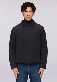 Quiltad mörkgrå jacka med krage, knäppning fram och textil med struktur, i kombination med blå denimjeans. Solitt utförande och modern passform.